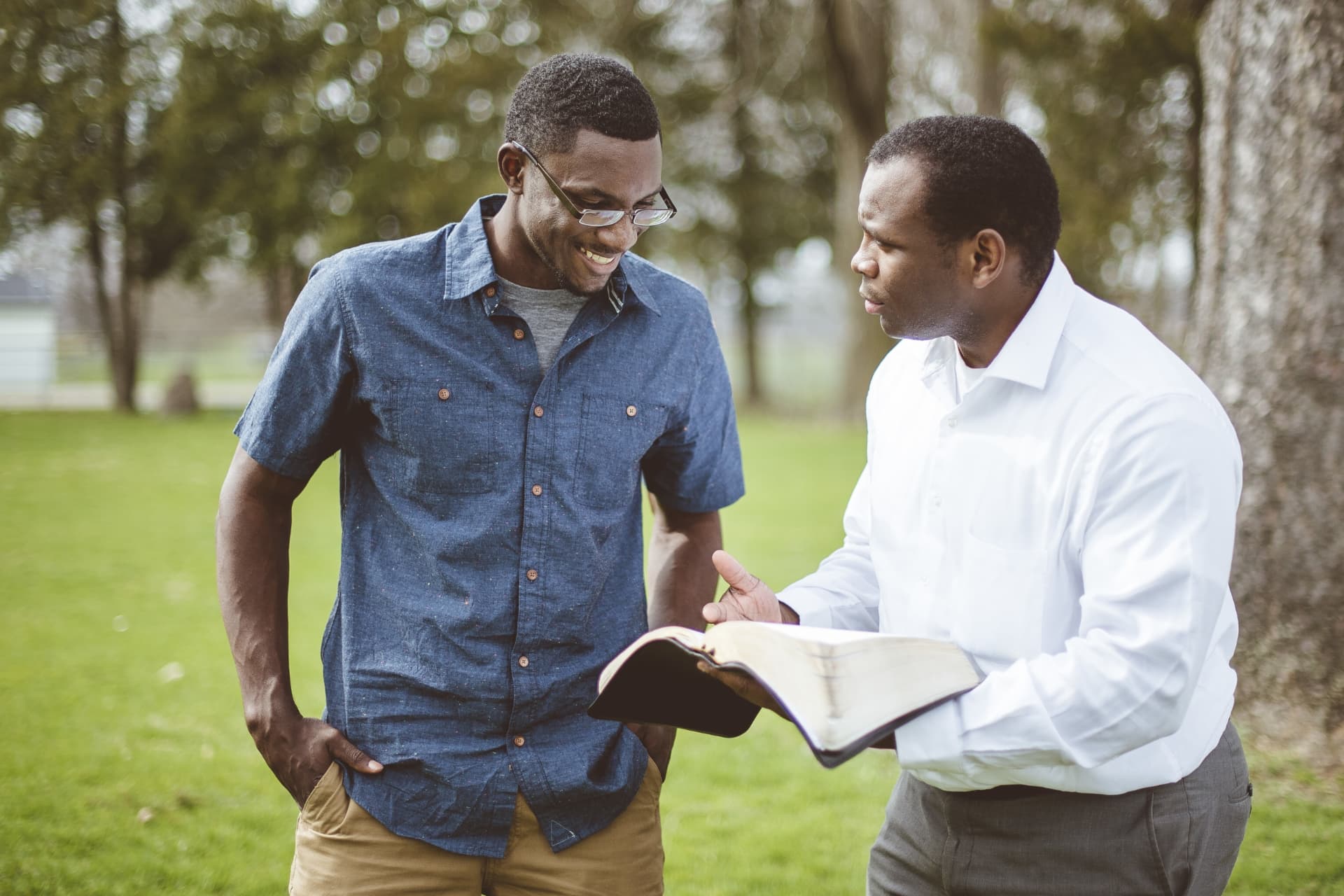 A man in a white shirt sharing an open Bible with another man outdoors